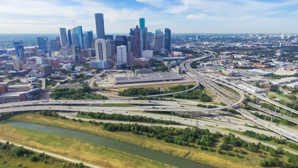 Aerial view of massive freeway interchange with downtown Houston skyline in background.