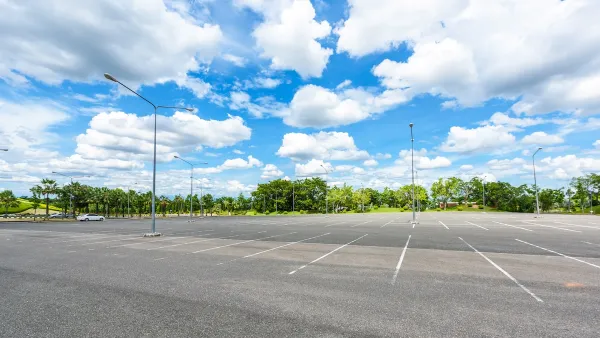 Empty large outdoor parking lot with green trees in background.
