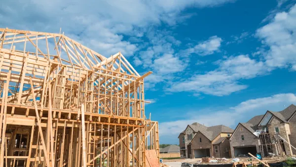 Wood-framed houses under construction with brick-covered completed homes in background.