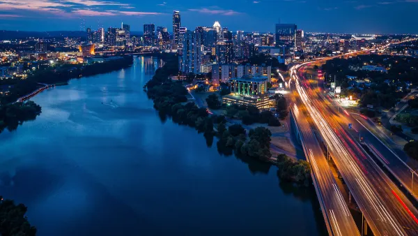 Aerial view of Interstate 35 with blurred traffic and Austin, Texas skyline in background with river in foreground at nighttime.