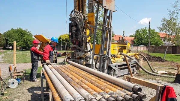 Workers next to excavator digging a geothermal well.