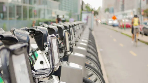 Close-up of silver Bixi bike share bikes parked at a station in Montreal, Quebec, Canada with blurred person on bike riding away in background.