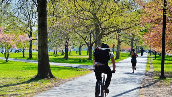 Cyclist and runner on paved bike and pedestrian path in a park in Boston with fall colors on trees.