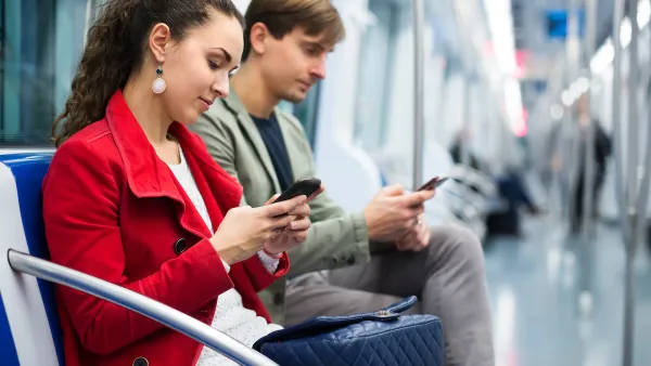 Young woman and man seated on subway car looking at phones.