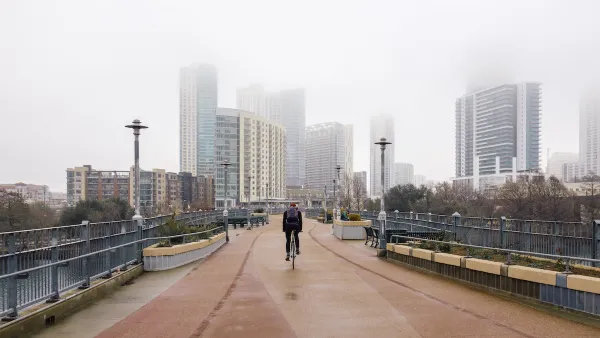 One cyclist rides on pedestrian bridge with foggy Austin, Texas skyline in background.