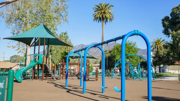 Blue and green playground equipment in Los Angeles with palm tree and mountains in background