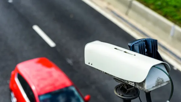 Close-up of speed camera mounted above roadway with red car passing by underneath