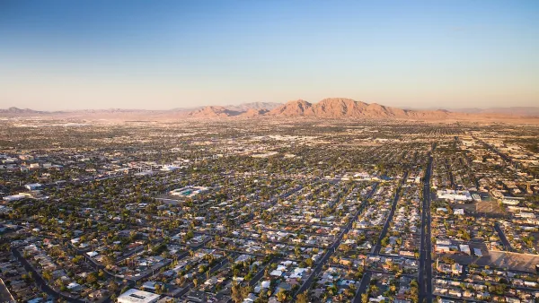 Aerial view of sprawling Las Vegas suburbs at golden hour with desert mountain in background.