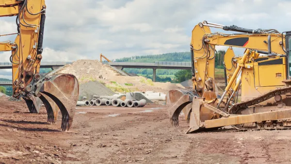 Three yellow excavators at a road construction site with elevated roadway in background.