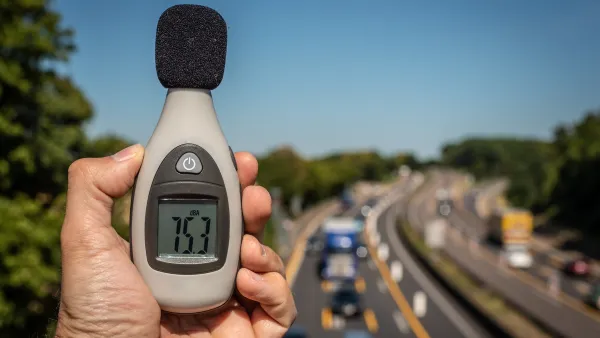 Close-up of hand holding up decibel meter with blurred highway with traffic in background