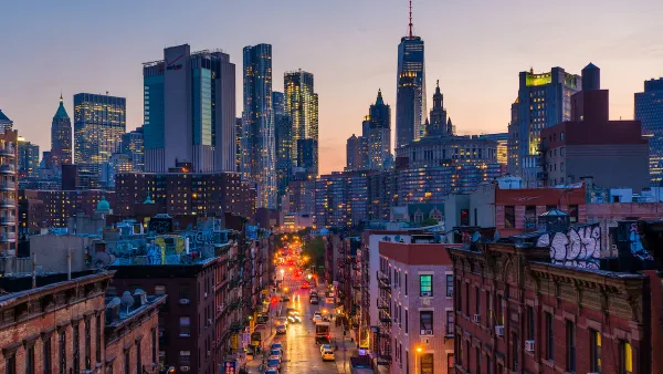 View down New York City street with rick buildings in foreground and modern skyline in background at sunset.