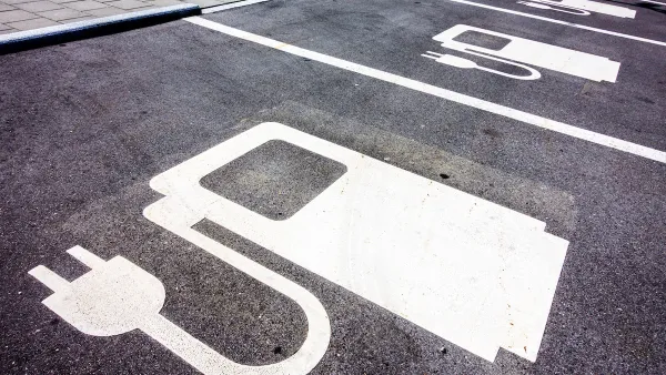 Close-up of white electric car charging symbol on black pavement in parking spaces.