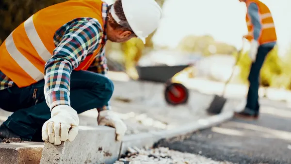 Construction workers in orange vests and white hard hats installing concrete curb.