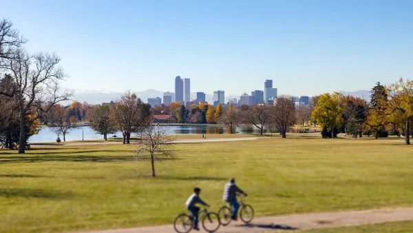 Two people on bikes on trail on green lawn with Denver, Colorado skyline in background.