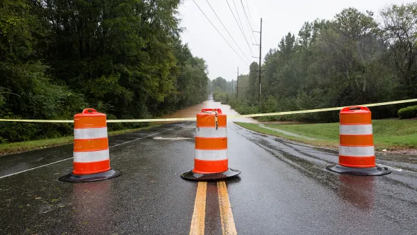 Orange and white barrels with yellow caution tape blocking flooded road.