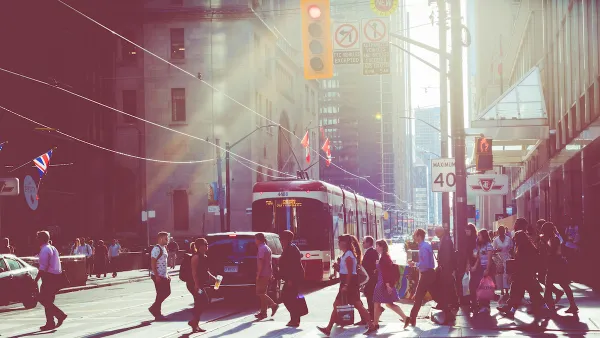 Pedestrians in busy crosswalk with tram in background in downtown Toronto, Canada with sunrise or sunset light in background.