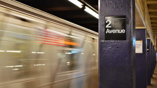 View of 2nd Avenue sign on concrete column on subway platform with blurred train speeding past in New York City.