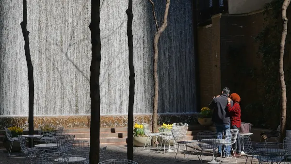 Man and woman watch waterfall in Paley Pocket Park in Manhattan, New York City. Park is filled with white tables and chairs.