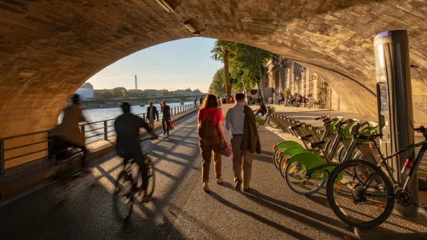 PEople on bikes, pedestrians, and a bike share station under Pont Neuf in Paris, France.