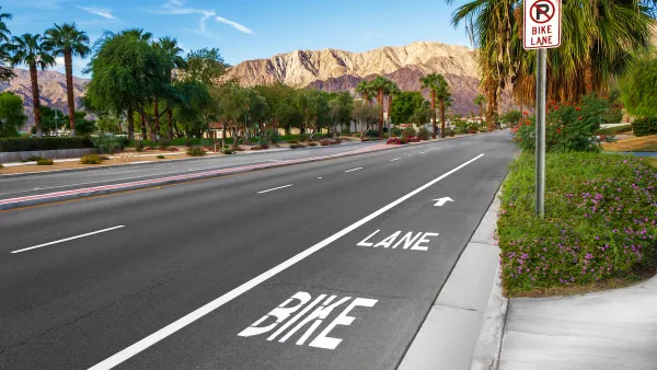 Marked bike lane on wide asphalt street with palm trees and Los Angeles mountains in background.