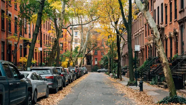 Small New York City street with brownstone homes and cars parked on one side.