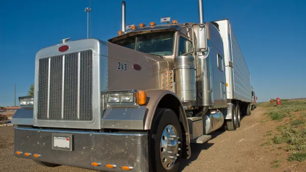 Front view of a tan semi-truck cab parked on a vacant piece of land with a clear blue sky in the background.