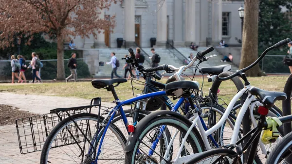 Close-up of crowded bike rack on university campus with students walking in background.