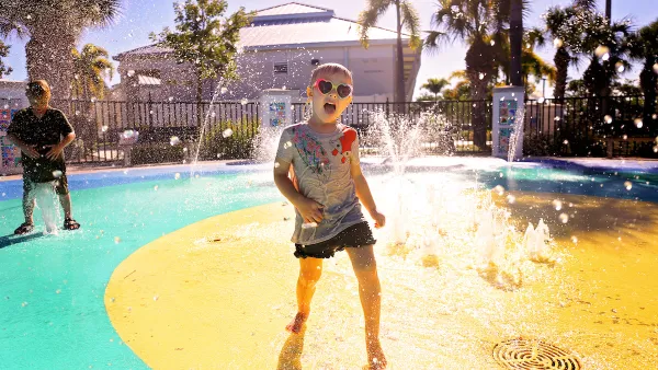 Child wearing heart-shaped sunglasses playing at splash pad in park.