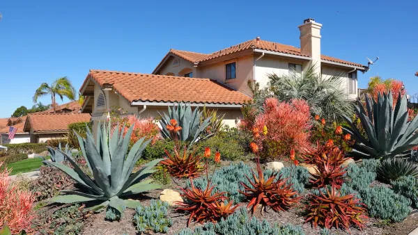 Drought tolerant desert plants including large agaves in the front yard of a Spanish-style Southern California home with red tile roof.