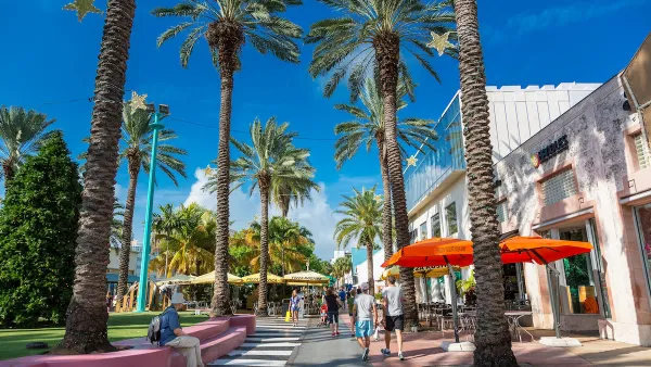 Pedestrian street with colorful patio umbrellas and tall palm trees in Miami, Florida.