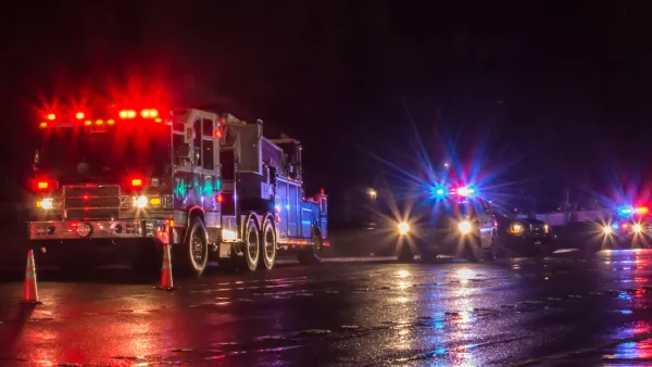 Nighttime view of fire truck and police cars with flashing lights on parked in a wet street