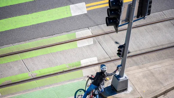 Cyclist pressing crossing button at green painted crosswalk.