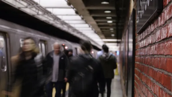 Busy New York City subway platform with blurred people walking in and out of trains and close-up on red brick wall on right.