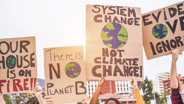 Close-up of signs calling for action on climate change being help up by multiple people outdoors.