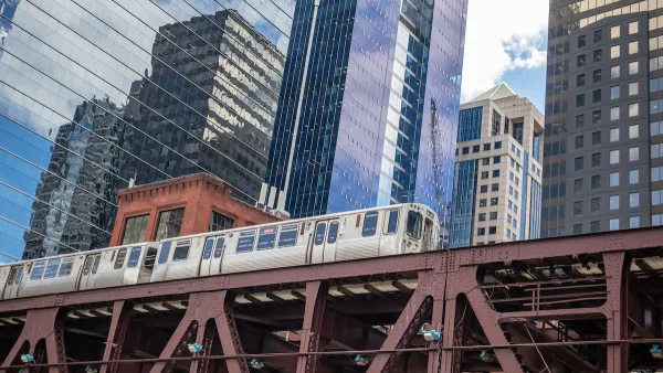 View up at Chicago elevated train line with train passing and glass high-rises in background.