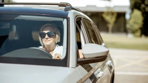 Senior woman wearing sunglasses sitting in the driver's seat of a silver car.