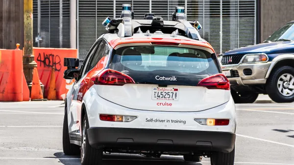 White and red Cruise self-driving car with "Self-driver in training" sign on back