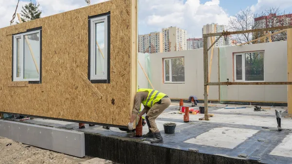 Worker in yellow construction vest working on modular home under construction.