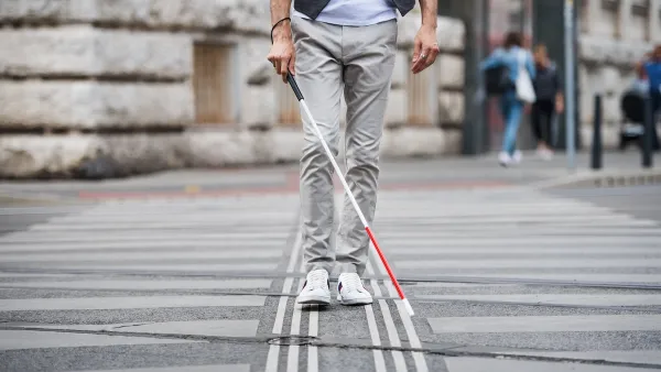 Low view of person with vision impairment cane walking through crosswalk.