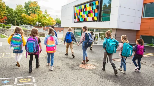 Group of children with backpacks walking toward colorful modern school building.