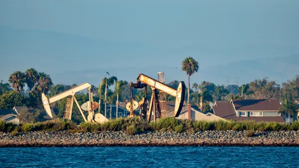 Oil drilling pumps on a wetland beach in California with houses in background