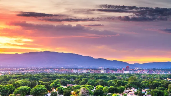 View of Albuquerque, New Mexico with green trees in foreground, mountains in background against sunset sky.