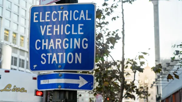 Close-up on blue and white "Electric vehicle charging station" sign with arrow pointing right on pole on city street.