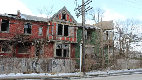 Vacant two-story red brick home in Detroit with missing windows.
