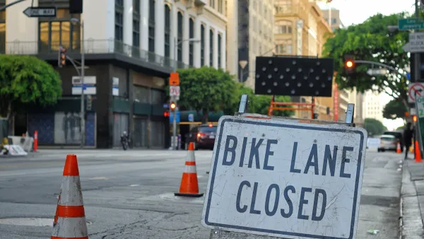 Close-up of Bike Lane Closed sign on street in downtown Los Angeles with orange traffic cones blocking lane in background.