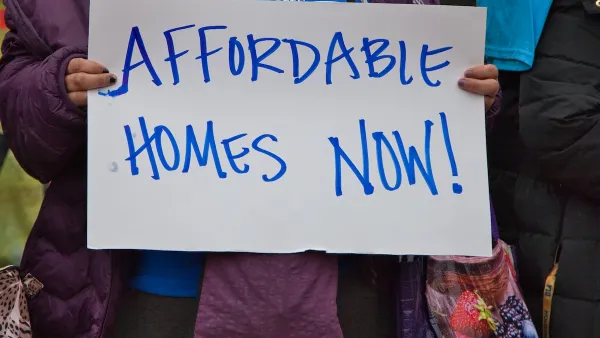Close-up of person holding hand-written "Affordable Homes Now!" sign.