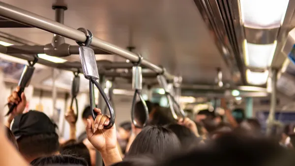 Close-up on passengers holding overhead straps on busy public transit bus.