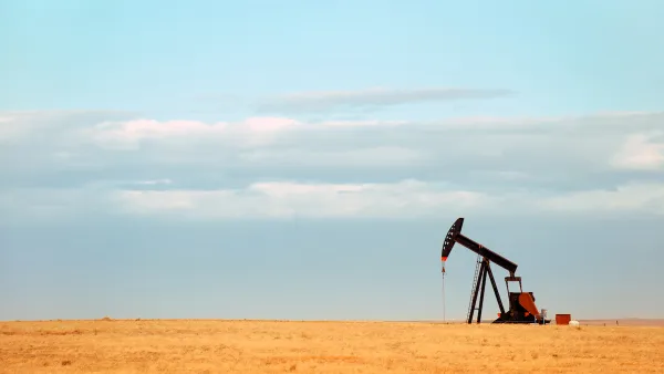 Single oil derrick on dry prairie with faded blue sky in background.