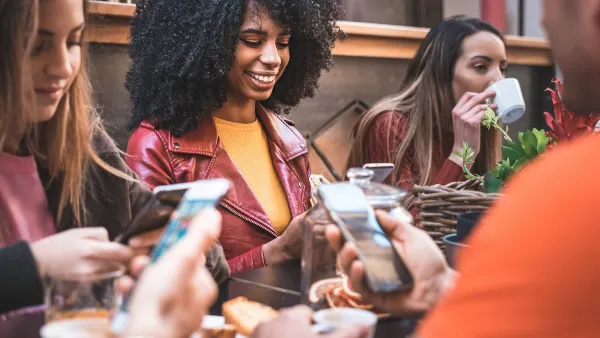 Close-up on group of young people sitting at a table using their cell phones.