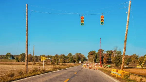 Two-lane rural road with stoplights hanging above roadway and construction visible in distance.